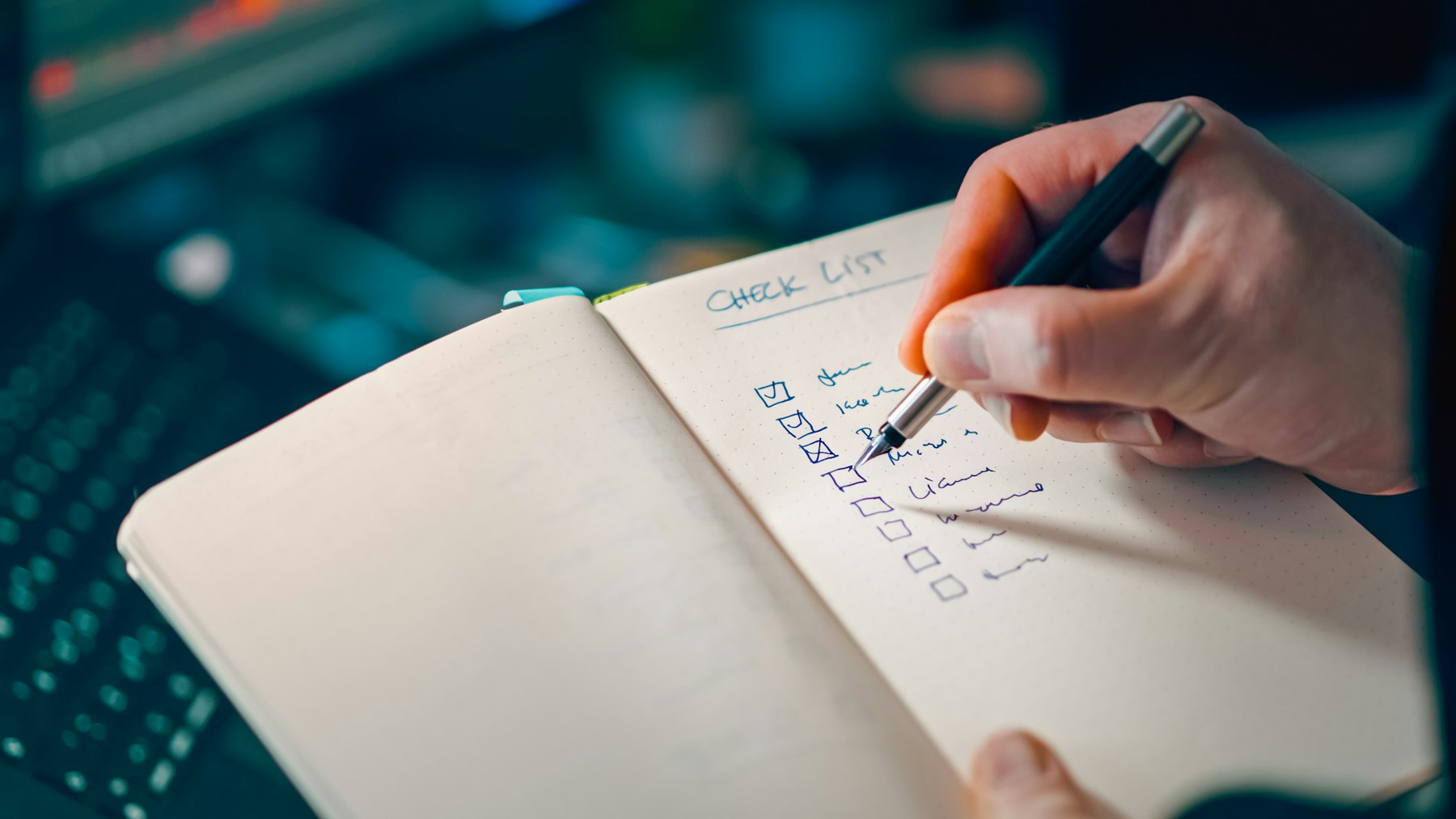 A hand with a pen ticking items on a handwritten checklist in a notebook beside a keyboard, standing in for scoring an agent on twenty real jobs
