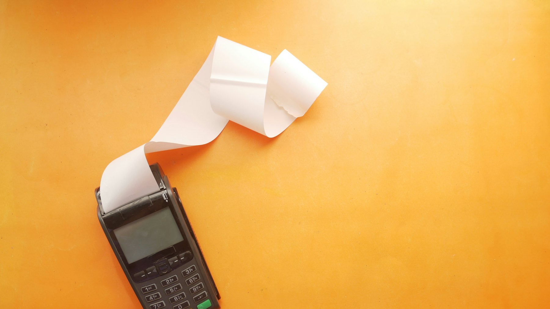 A black card payment terminal with a long blank paper receipt curling out of it, standing in for outcome-priced AI agent business ideas
